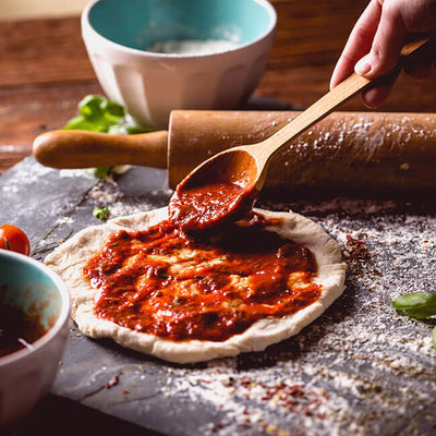 Der ausgerollte Pizzateig wird mit Pizzasoße kreisförmig eingestrichen. Die Soße wurde aus Neapels Pizzatomten hergestellt und zwar die San Marzano Dosentomaten.