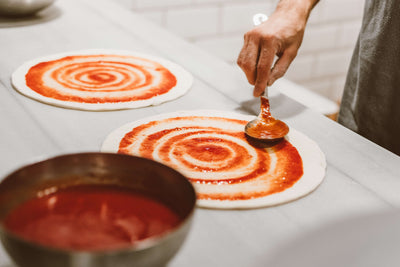 Pizzabäcker bestreicht den ausgerollten Pizzateig mit San Marzano Tomaten für eine kraftvolle Pizza. 