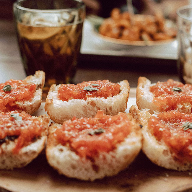6 Bruschetta auf einem Holzbrett. Für den Belag wurde Datterini Tomaten verwenden auch als Datteltomaten oder Kirschtomate bekannt. Ihr feuriges Rot auf dem hellen Brot erzeugt einen leckeren und intensiven Kontrast